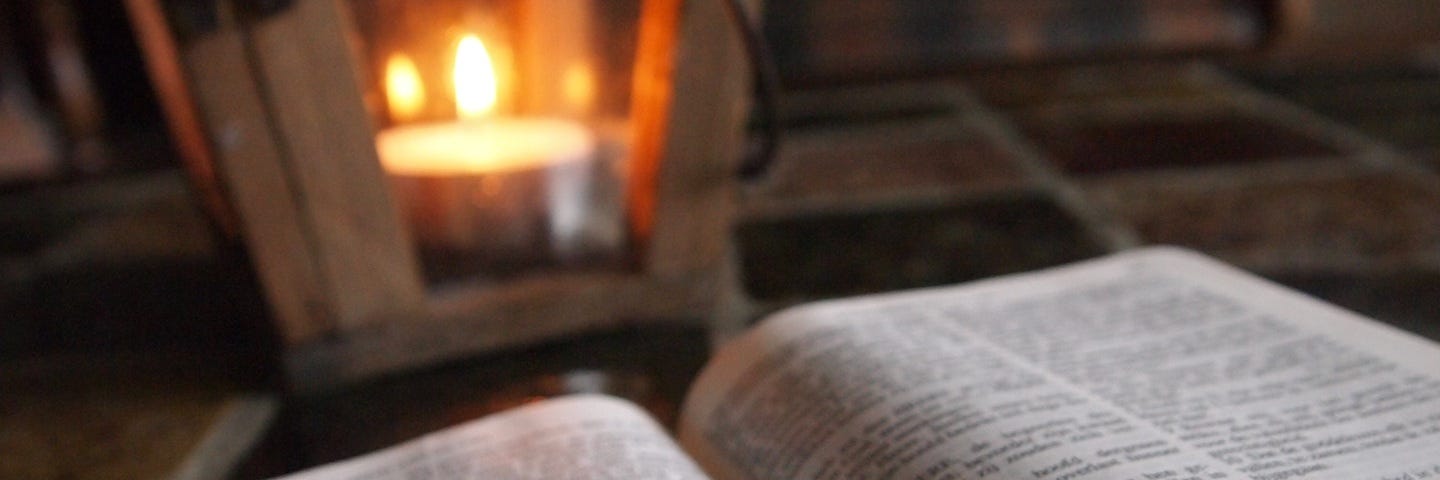 A bible lying open, lit by a candle