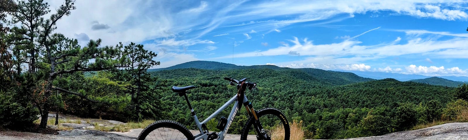 Photograph of the author’s Santa Cruz Hightower on Big Rock Trail in DuPont Forest. The bike is standing alone on bare rock along a ridge line with green trees and clear blue sky in the background.