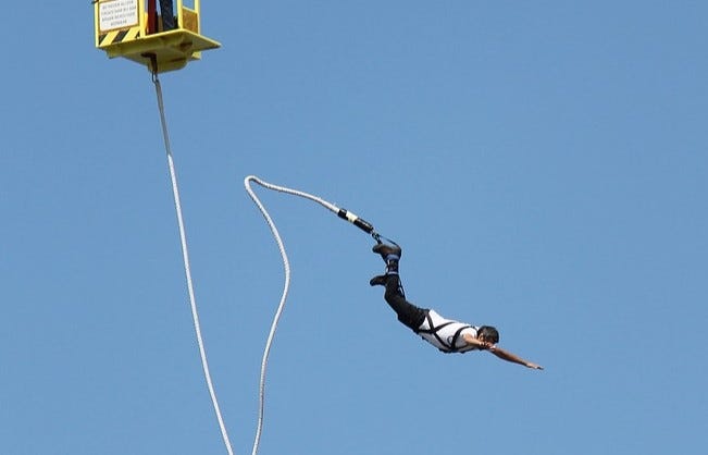 Person jumps headfirst, like Superman, from bungee platform, harness around feet.