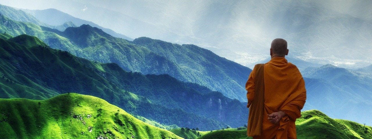 Buddhist monk looking over some green hills and mountains.