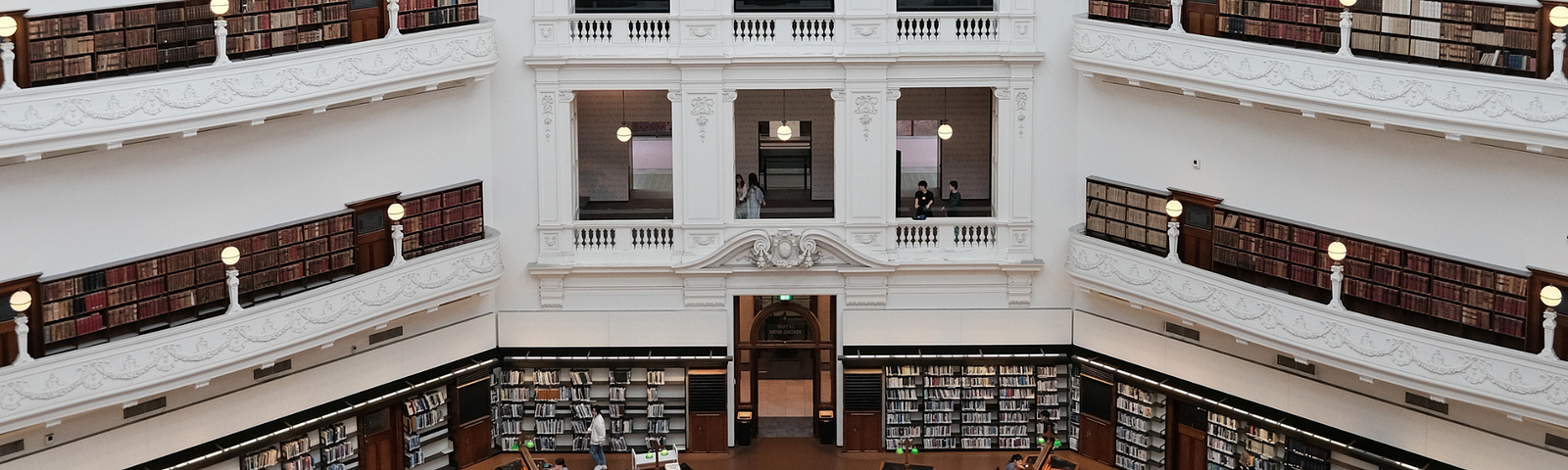 A photo of a grand library reading room with people working at desks and browsing books on shelves
