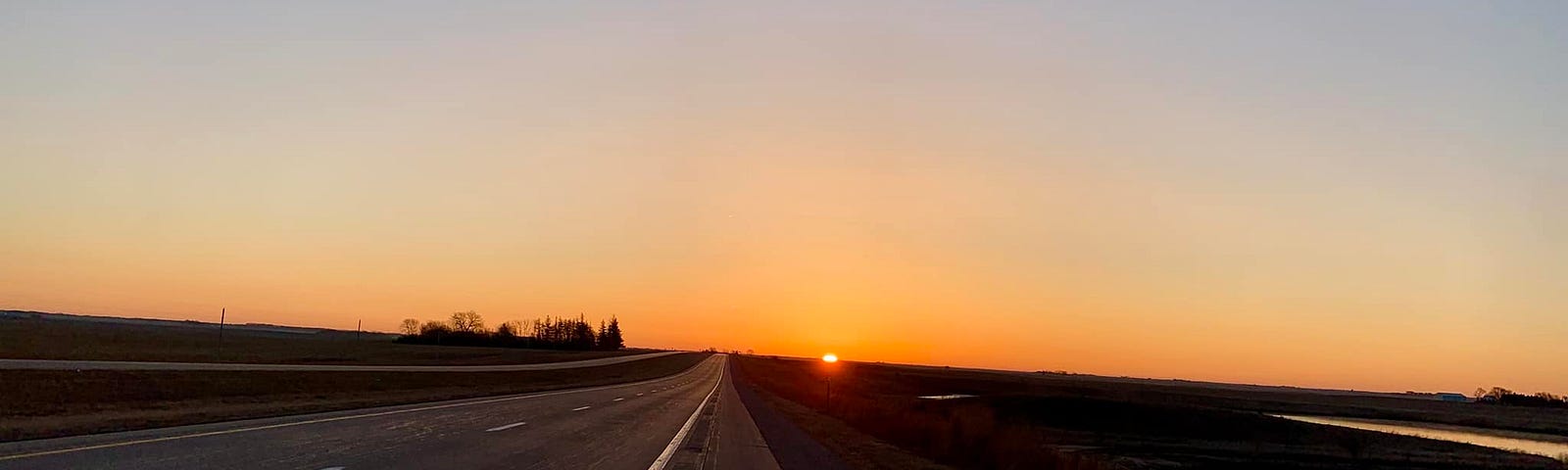 Landscape photo of the sun coming up over an empty highway.