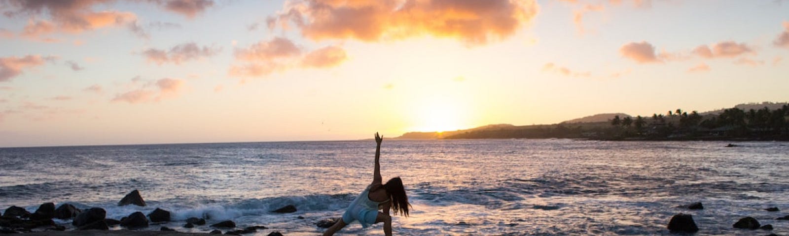 Woman doing yoga on the beach beside the ocean with the sun setting behind her. Chanting OM benefits the body, mind and soul