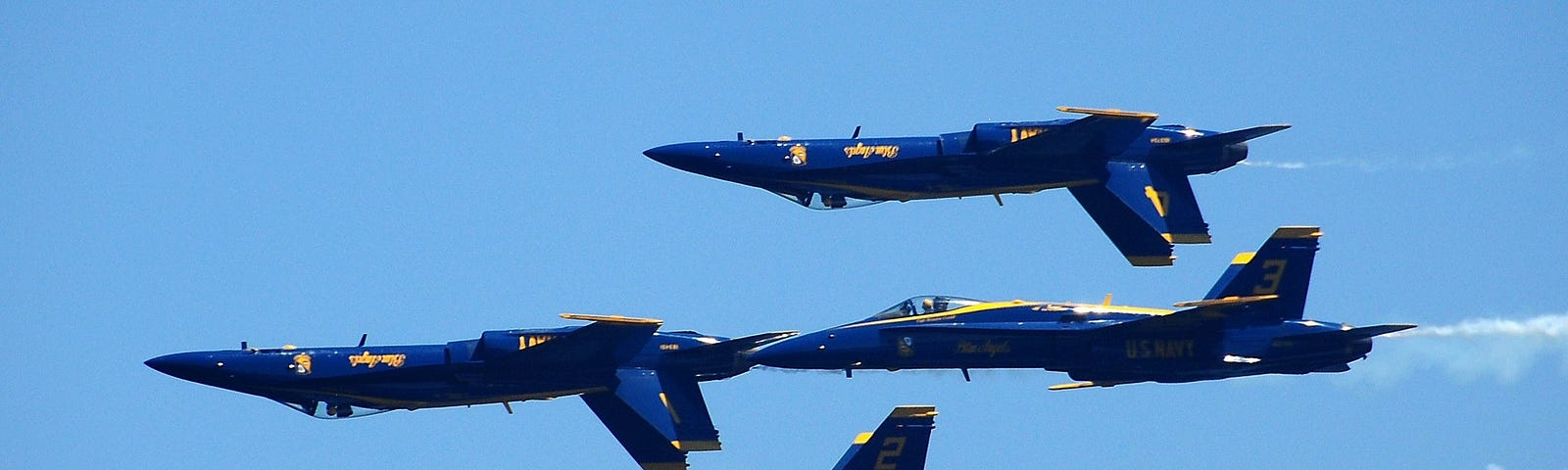 Four blue milltary jets in a tight acrobatic formation