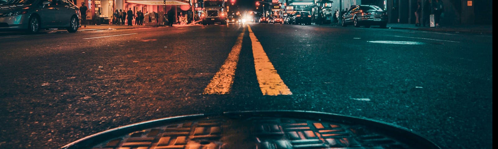 Night scene of a man-hole in the centre of a street with building lit up either side of the road