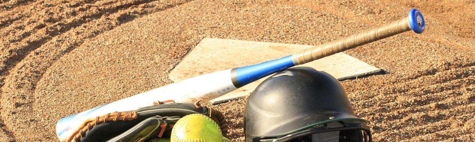 Photo of home plate with a bat, some baseballs and a batting helmut nearby.