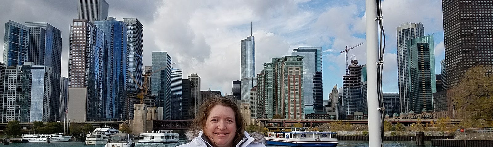 An obese white woman with medium brown shoulder-length hair stands on a boat with the Chicago skyline in the background.