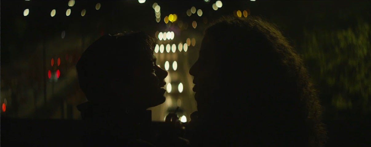 two young people facing each other in silouette at night, street lights can be seen behing them
