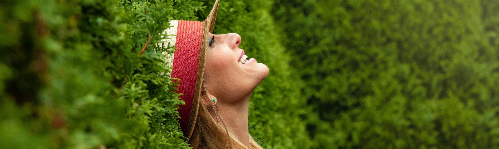 A happy, vital woman wearing a hat smiles in the garden.