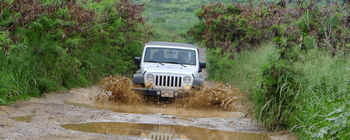 Jeep driving through large puddles of water on a dirt road in Kauai
