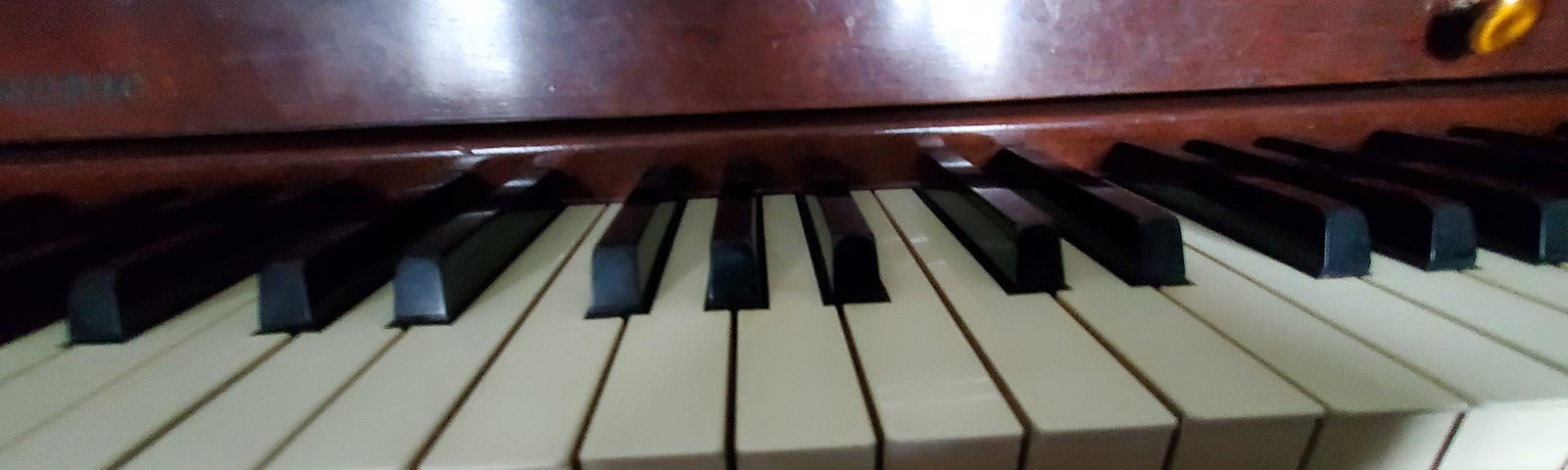 Closeup of black and white piano keys. The wood behind the keys shines with a glare from sunlight.