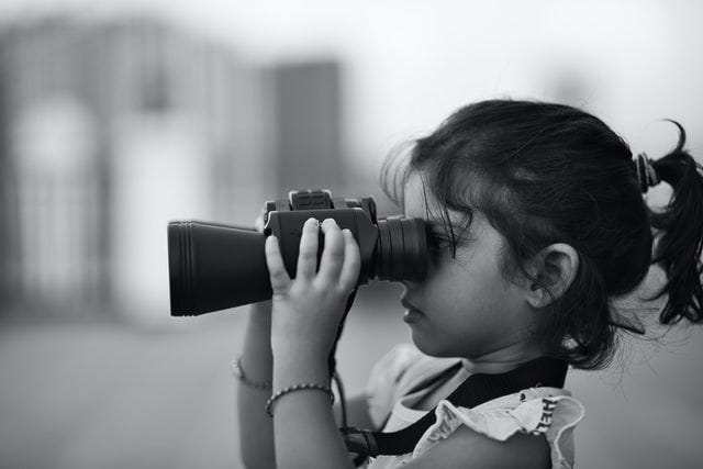 A photograph of a young girl looking through binoculars.