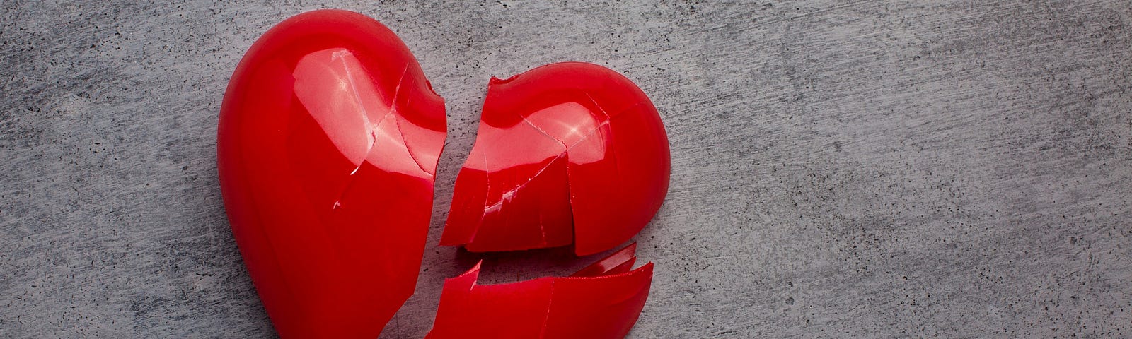 This photo shows a red plastic heart that is broken into three pieces.