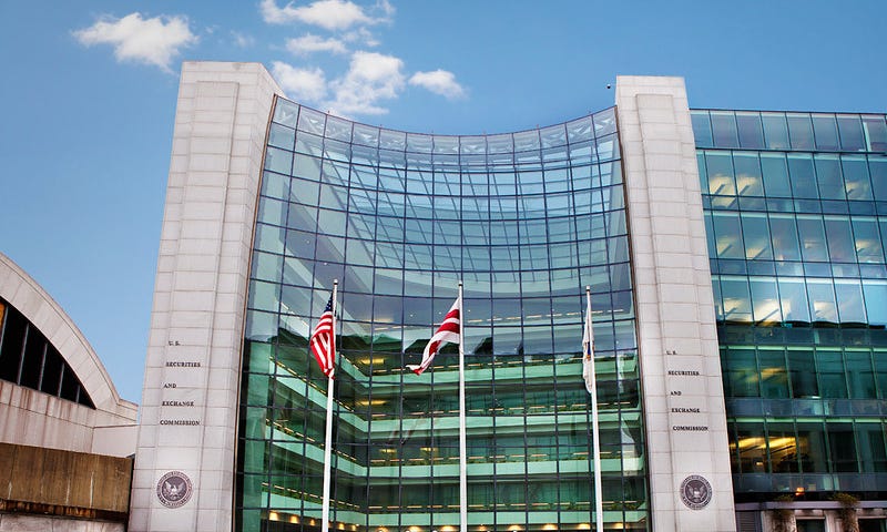 This photo is a picture of the exterior of the U.S. Securities and Exchange Commission headquarters. It is a glass-paneled building with two large cement columns that read, “U.S. Securities and Exchange Commission.”