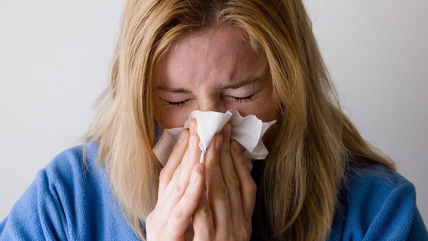 IMAGE: A sick blonde woman on a blue robe blowing her nose