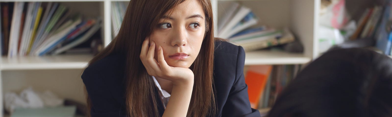 Teenage student sitting at desk in classroom with chin resting on her hand