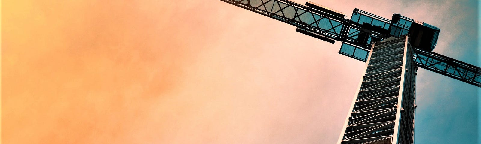 A huge crane in front of a building under construction, with the rising sun in the background.