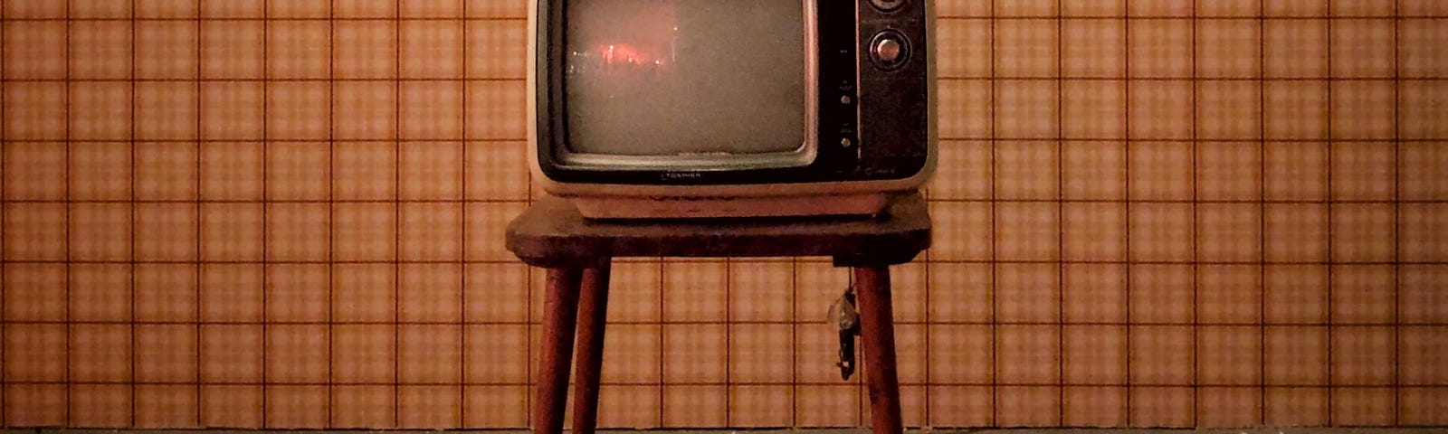 Vintage TV on a wooden table. Gray carpet underneath and a plaid striped background.