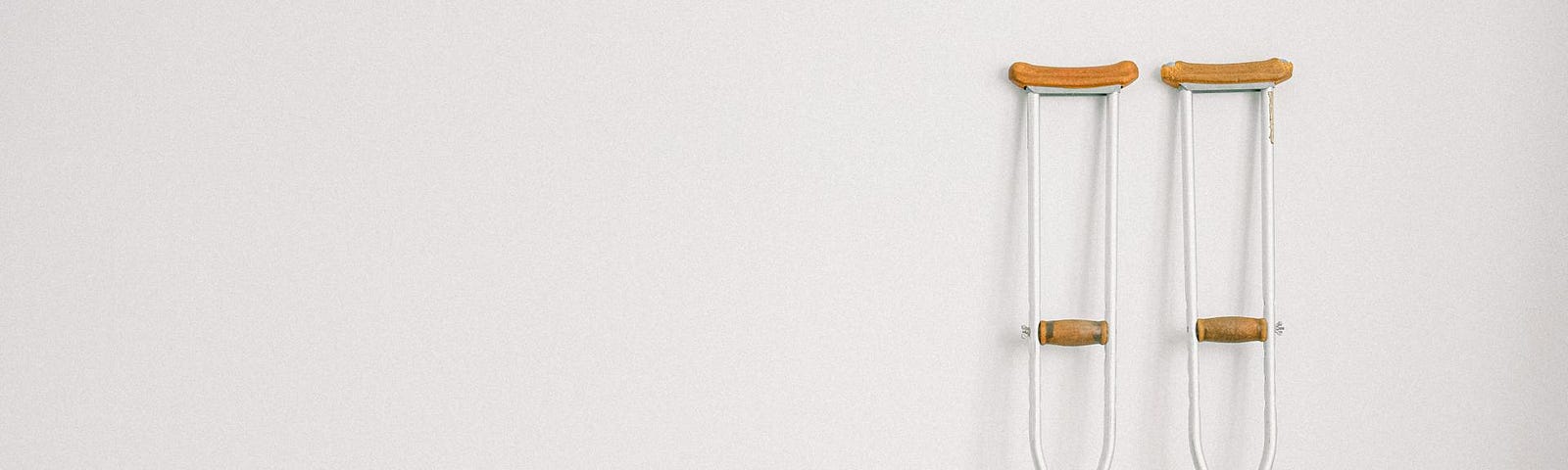 A pair of crutches rests upright on a white wall.