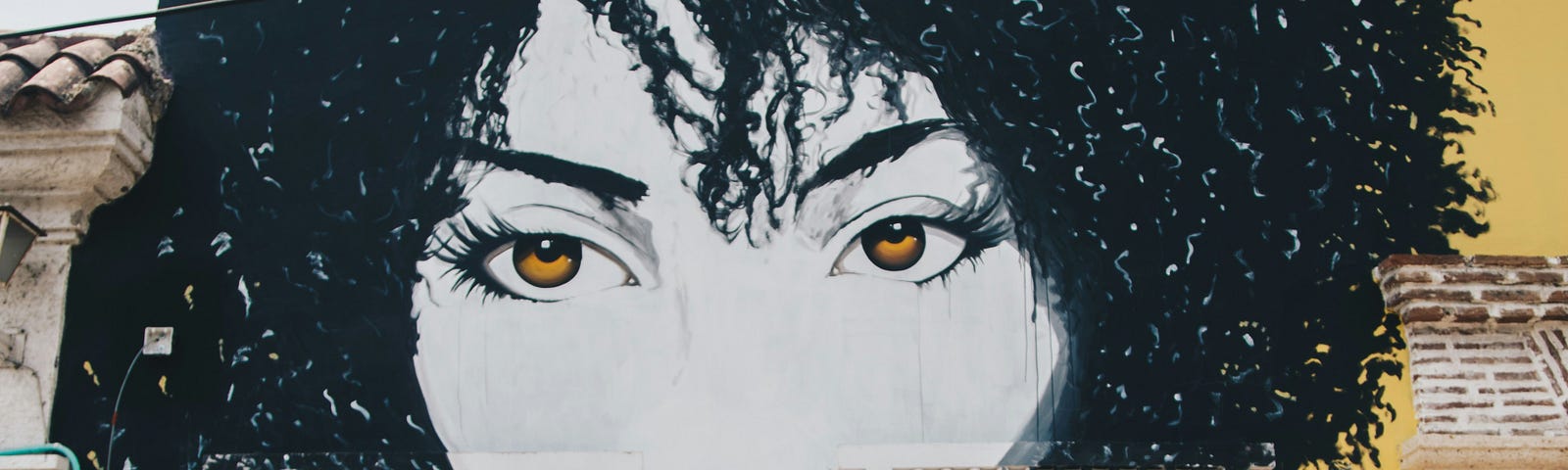 murial painting of woman on the side of a building. She has black curly hair and brown eyes and red lipstick.