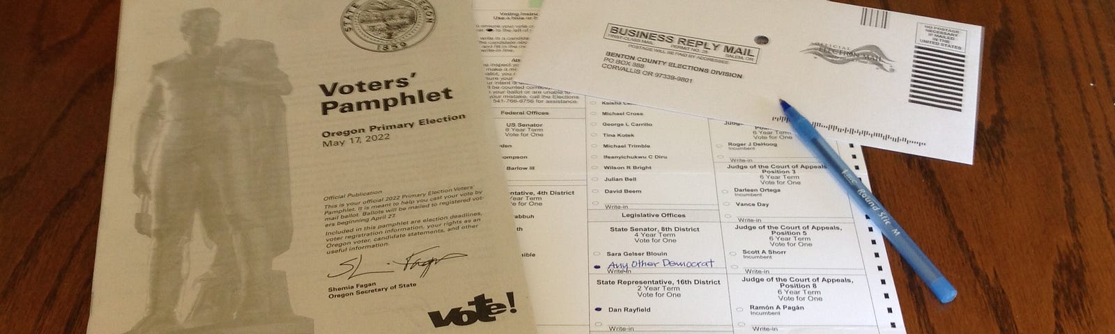 Photo shows a ballot, voter’s pamphlet, ebvelop and pen on a dining room table.