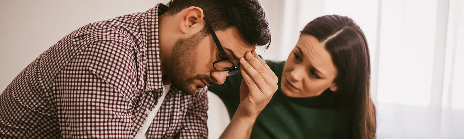 A woman consoles her male partner while sitting next to him. Her hand rests gently on his head.