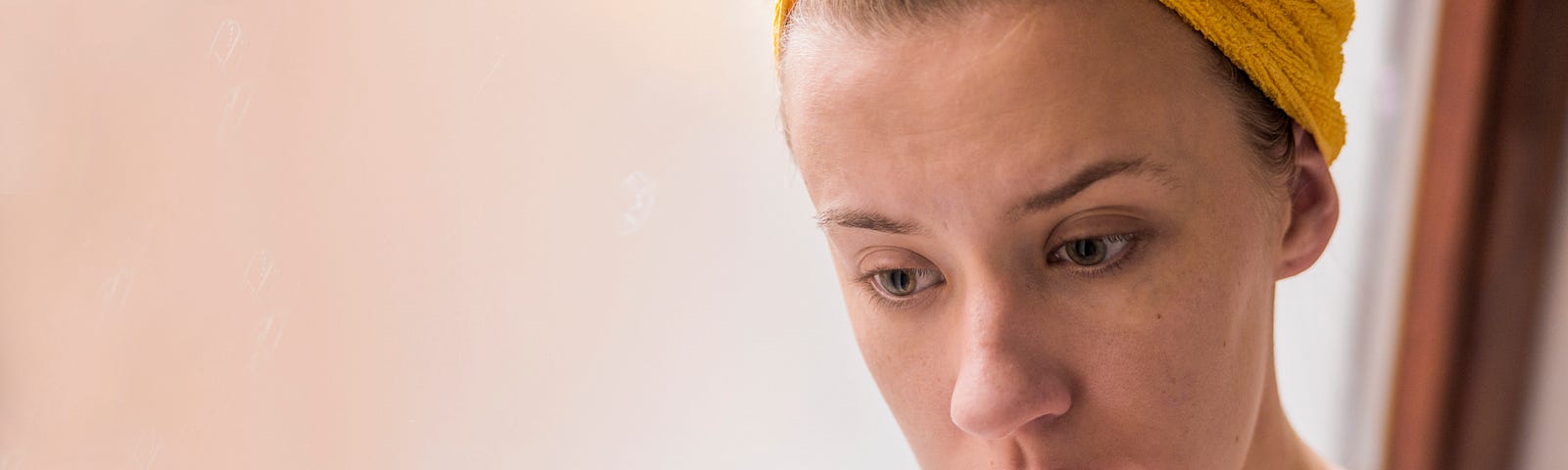Head and shoulder shot of a sad young woman wearing a yellow wrap on her head. She looks desperately worried and is biting the nail of her index finger.