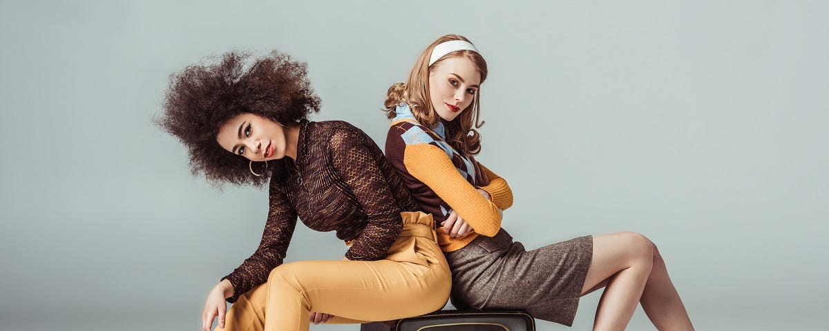 Two cool looking retro girls sitting on an old-fashioned TV.