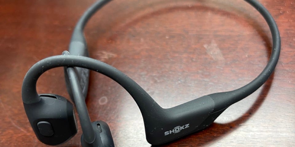 Shokz Open Run Pro headphones placed on a wooden surface showing their size and look.