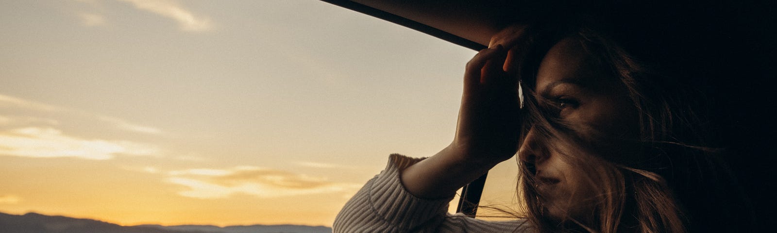 A woman looking out a car window off into the distance pndering a question.