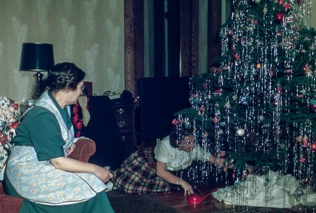 A mother watches her child decorate a Christmas tree.