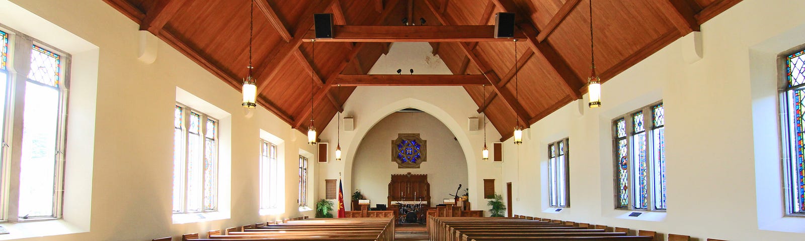 The interior of a church with wooden ceiling, pews, and windows on both sides of the wall.