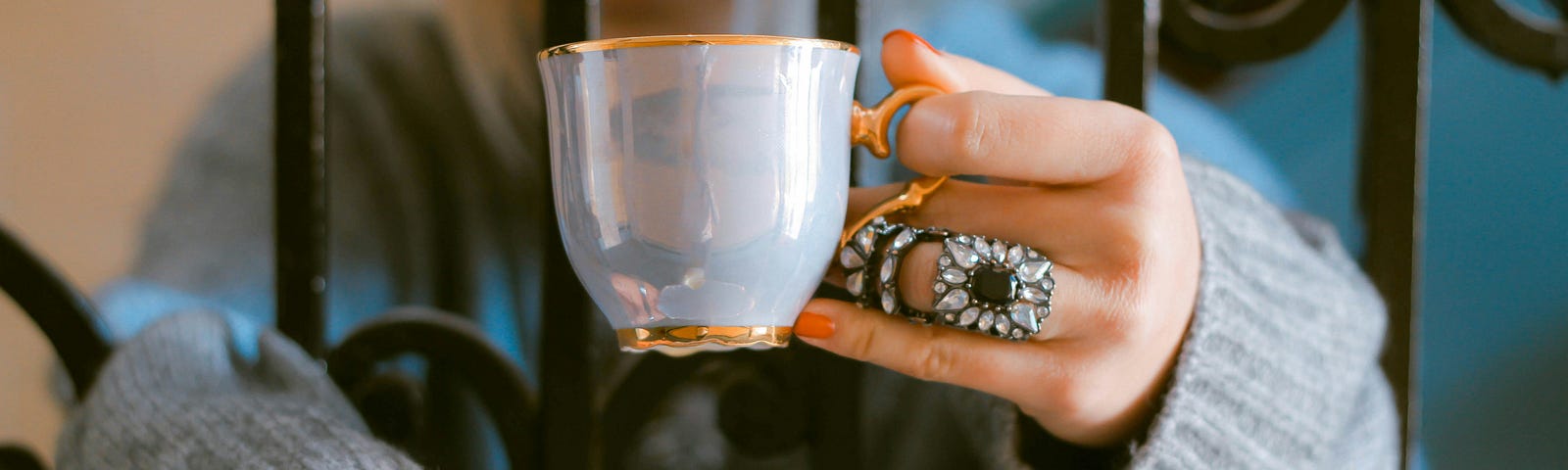 A tea cup and a saucer held by a person wearing rings on her hand