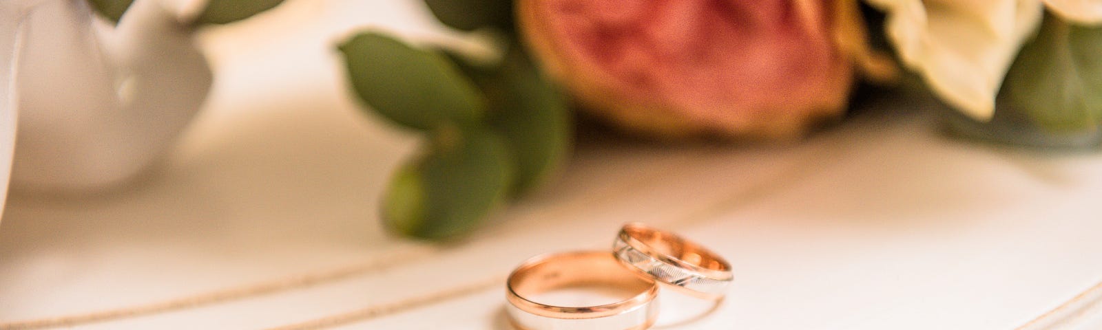 Two wedding rings on table with roses in background.