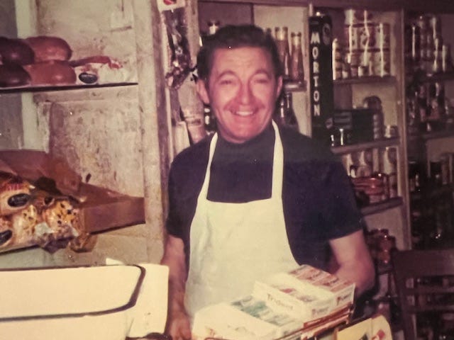 Photo of a grocer in a white apron smiling behind the counter