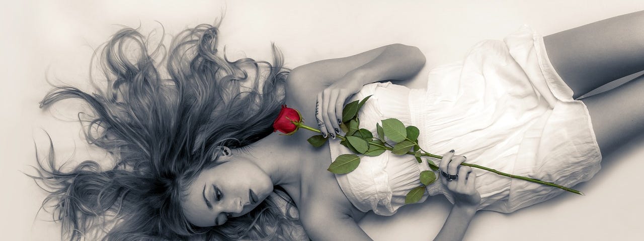 Beautiful young woman lying down with a rose on her chest