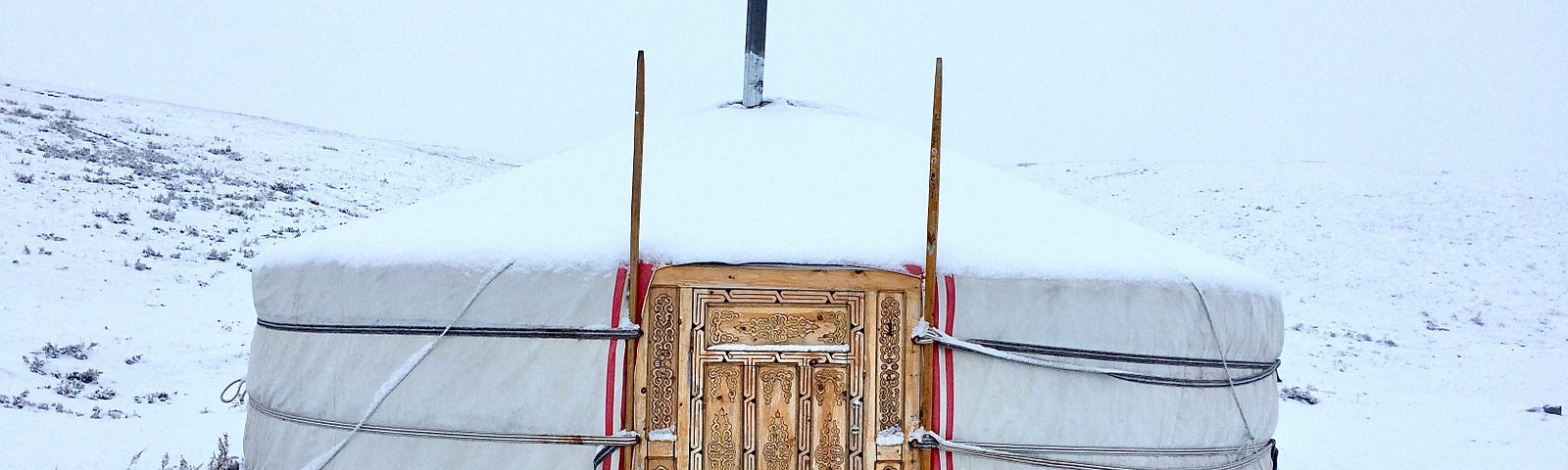 A snowy white yurt with a wooden door.