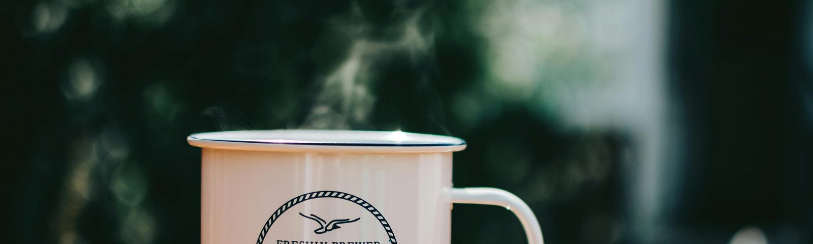 A coffee mug on a table set against background greenery