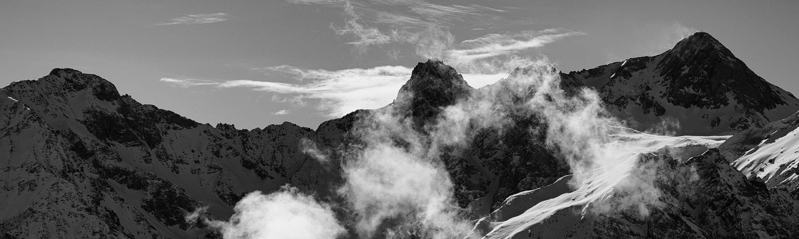 A mountain peak, kissed by thick clouds. Sunlight illuminates the summit, while the clouds dance and slowly drift down