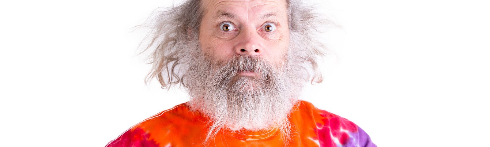 Senior man with grey hair and beard so surprised he’s wide-eyed, he is wearing a tie dye colorful t-shirt