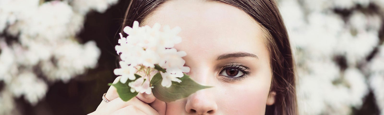 A woman in a red dress holds a flower in front of her face in a close-up photo.