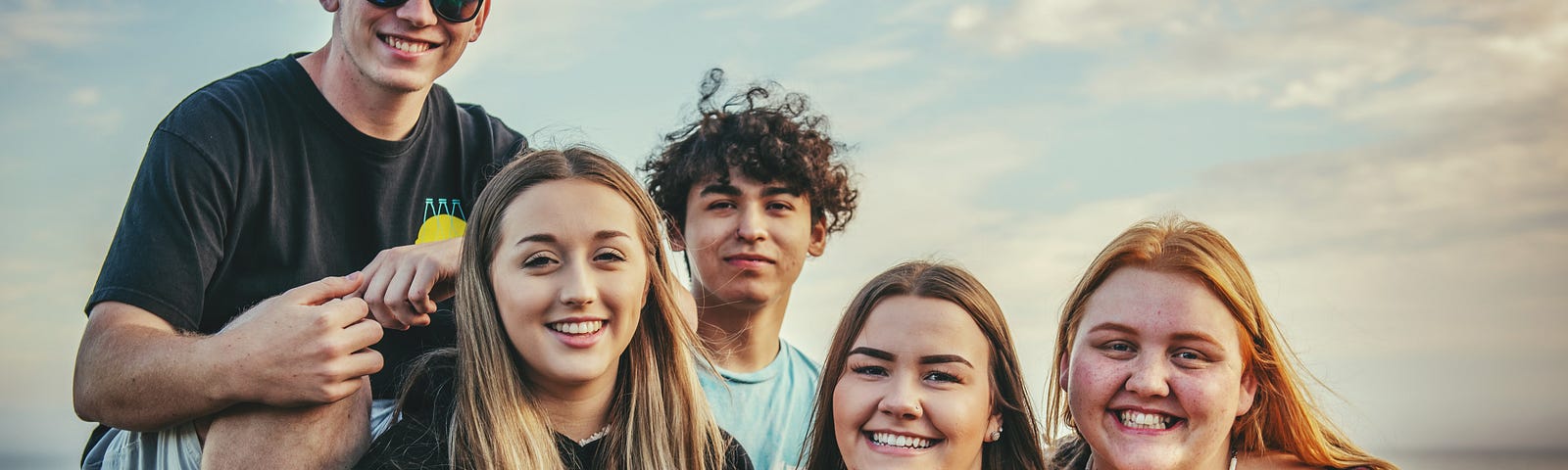 A group of five teenagers on the beach. Two boys and three girls.