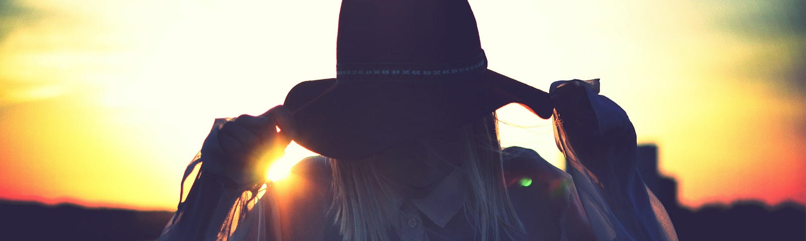 Woman with hat covering her face in front of sunset