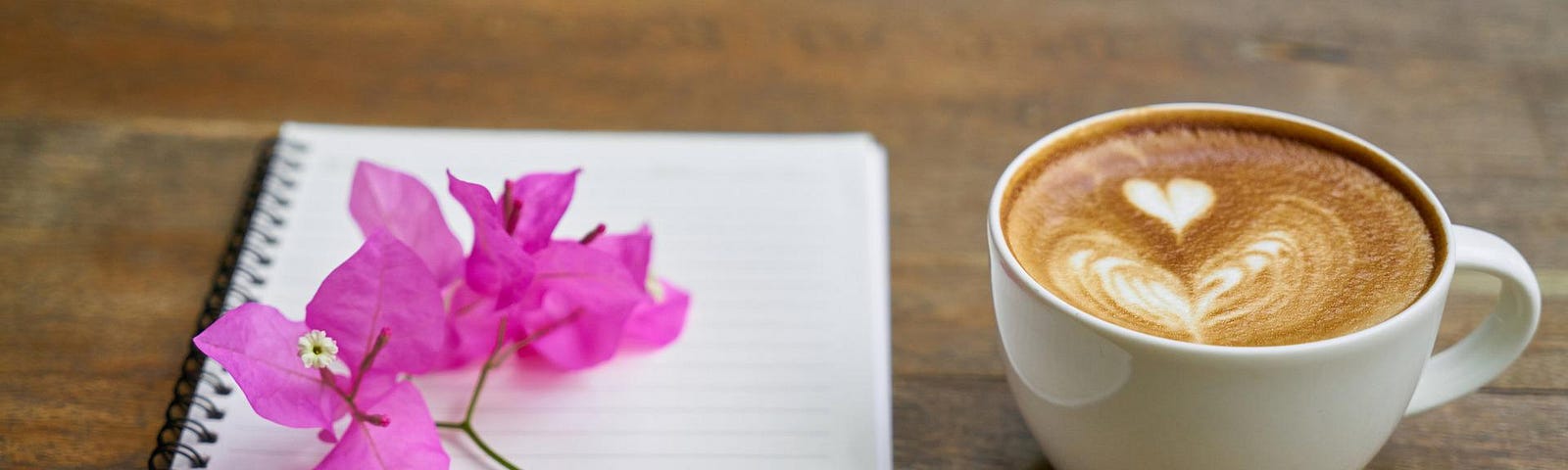 A lined notebook, pink flower and a cup of coffee