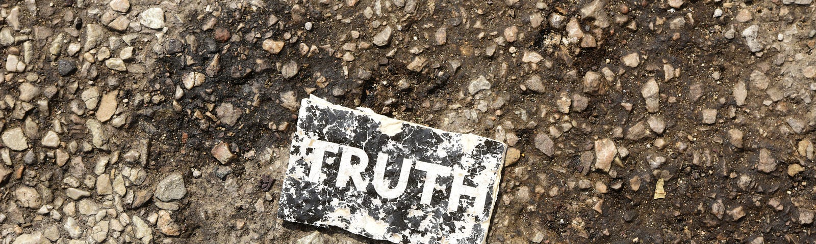 The word “truth” is printed on a dirty, trampled card, which lies on muddy gravel.