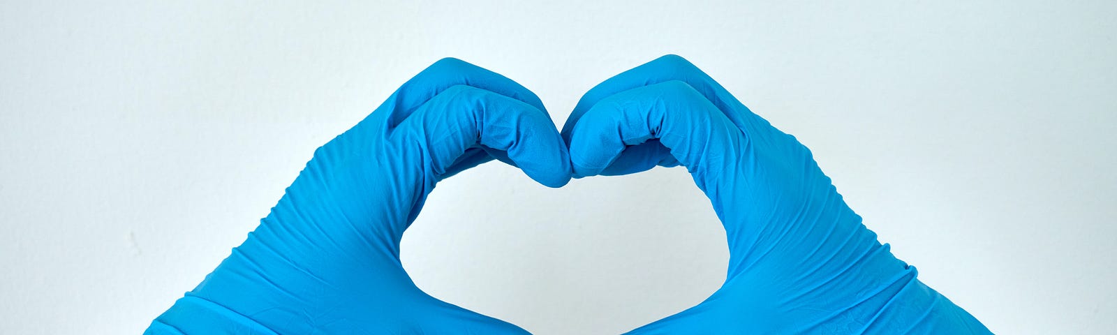 Two hands covered by blue, plastic gloves making the heart sign