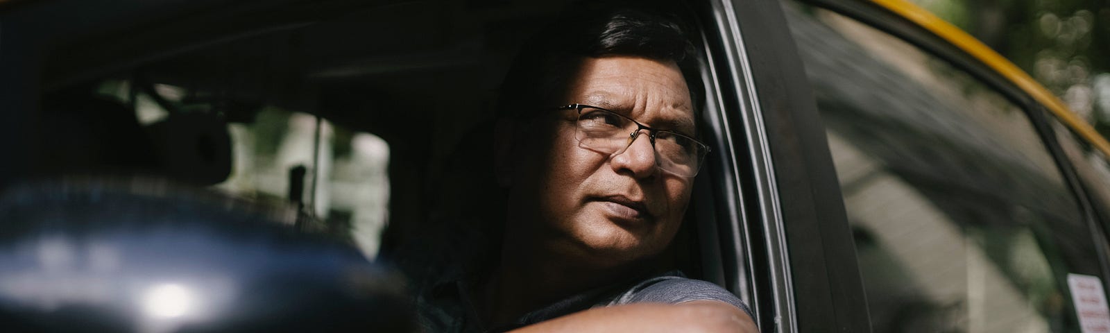 Serious ethnic male driver looking at opened window of taxi