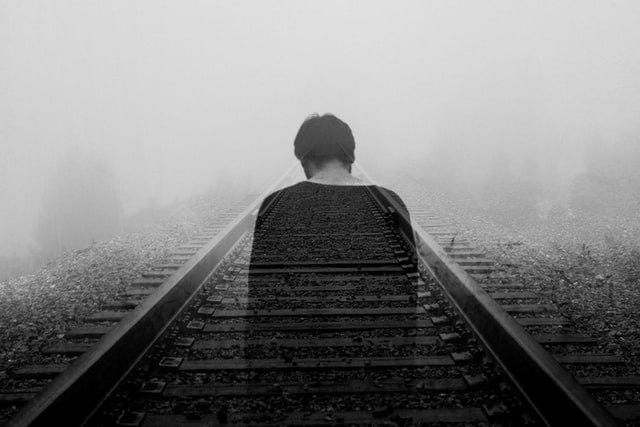 a black and white picture of a shadowing man walking on train tracks.