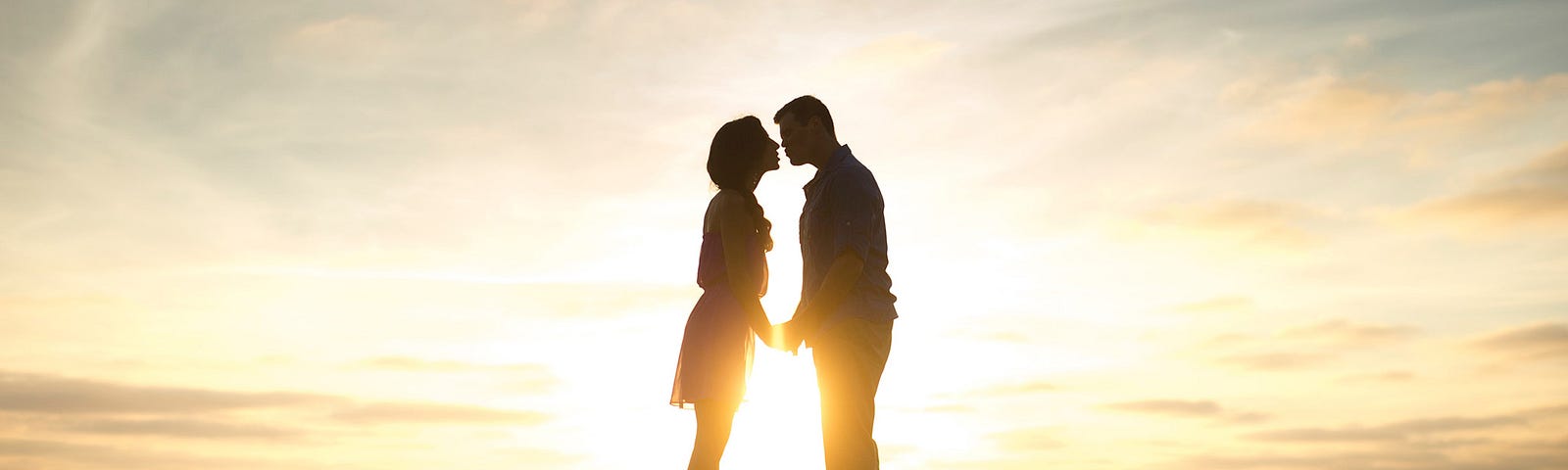 Couple standing on hill about to kiss with sunset in background