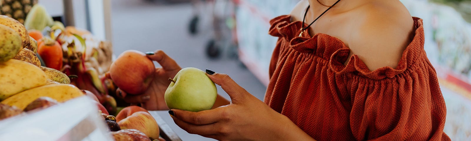 Young woman holding a green apple and an orange in the super market